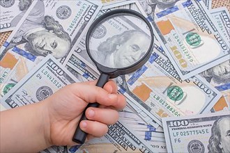 Magnifying glass is held over the banknote bundle of US dollar
