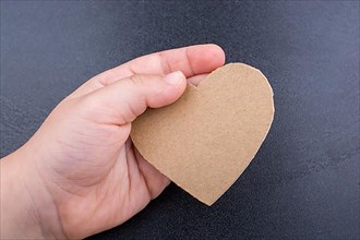 Heart shaped object in hand on a wooden black background