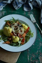 Vegan cauliflower salad on a tin plate with black cumin on a rustic table