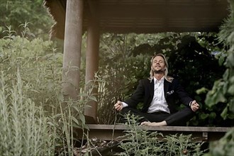 Businessman does yoga on wooden walkway in nature,