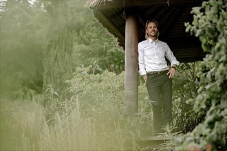 Businessman in a white shirt stands on the wooden jetty in the greenery,