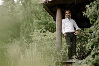 Businessman in a white shirt stands on the wooden jetty in the greenery,