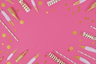Party flat lay with golden and white decoration like confetti and feathers forming border around pink background,