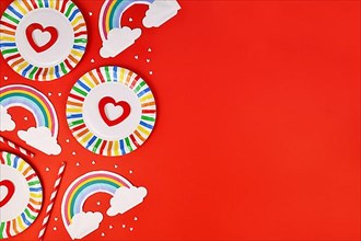 Party flat lay with colorful plates, rainbow napkins and drinking straws on red background with copy space
