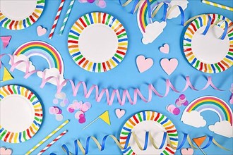 Party flat lay with colorful plates, rainbow napkins and drinking straws on blue background