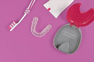 Customized transparent teeth bite guard clear aligners for lower jaw with storing case, tooth brush and paste on pink background