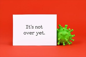 Corona virus model and note with text 'It's not over yet' on red background,