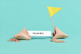 Fortune cookie with motivational text saying 'You can do it' with flag on real blue background,