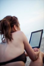 Woman on beach in bikini reading on tablet computer,