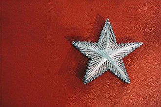 A star made from steel nails and string on a red background,