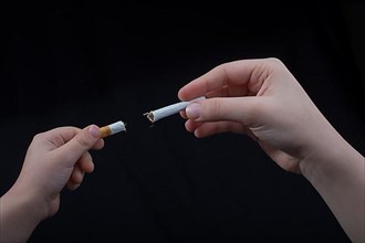 Hand is breaking a cigarette on a black background,