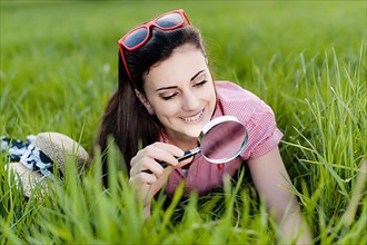 Young woman lying in meadow with magnifying glass,
