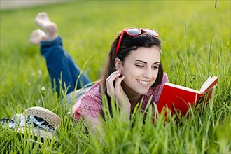 Young woman lying in meadow and reading a book,