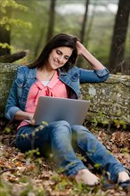 Young woman sitting in the forest with laptop,