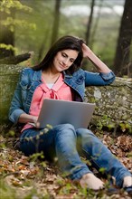 Young woman sitting in the forest with laptop,
