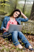 Young woman sitting in the forest with laptop,