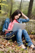 Young woman sitting in the forest with laptop,