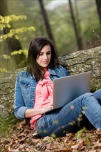 Young woman sitting in the forest with laptop,