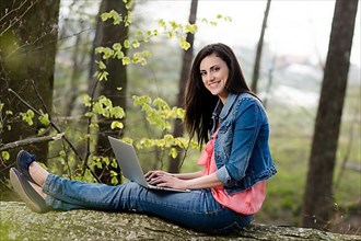 Young woman sitting in the forest with laptop,