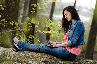 Young woman sitting in the forest with laptop,