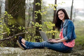 Young woman sitting in the forest with laptop,