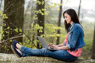 Young woman sitting in the forest with laptop,