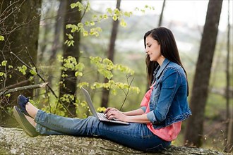 Young woman sitting in the forest with laptop,