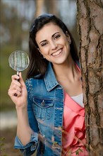 Woman looks at tree trunk under the magnifying glass,