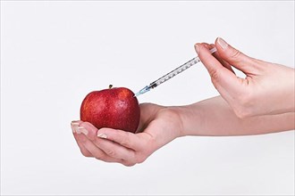 Apple being injected with syringe. Held by female hand,