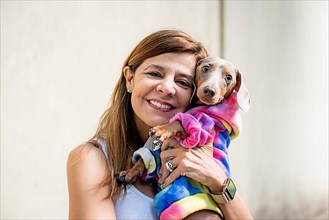 Latin woman holding her dog. Both are dressed alike and looking at camera,