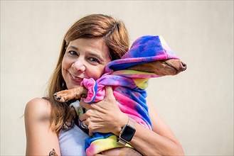 Latin woman holding her dog both dressed alike. She is looking at camera,