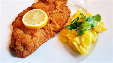 Delicious golden-brown fried Wiener Schnitzel with potato salad and a slice of lemon on a white plate,