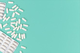 White capsule pills on left side of mint green background with blank copy space,