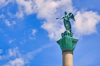 Sculpture of Roman goddess Concordia at top of column monument called Jubileumssaeule in front of blue sky,