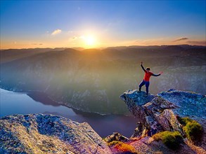 Woman standing with spread arms on a rocky outcrop at Kjerag above the Lysefjord, sunset