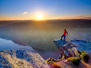 Woman standing on a rocky outcrop at Kjerag above the Lysefjord, sunset