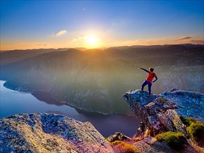 Woman standing on a rocky outcrop at Kjerag above the Lysefjord pointing her finger into the distance, sunset