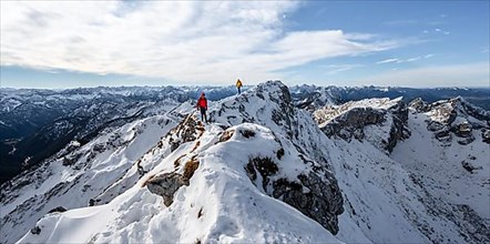 Two mountaineers on a narrow rocky snowy ridge, behind peak crow