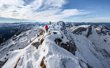 Two mountaineers on a narrow rocky snowy ridge, behind peak crow