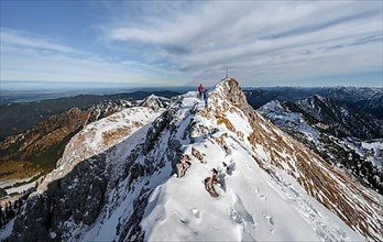Two mountaineers on a narrow rocky snowy ridge, in the back summit of the Ammergauer Hochplatte with summit cross