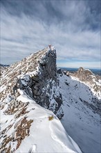 Mountaineer stretching his arms in the air, standing on a snow-covered rocky ridge