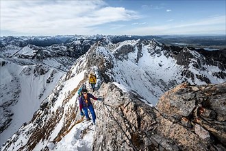 Two mountaineers on a rocky snow-covered ridge, the path is secured by a wire rope