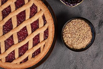 Close up of pie called Linzer Torte, a traditional Austrian shortcake pastry topped with fruit preserves and sliced nuts with lattice design next to bowl with ground almonds