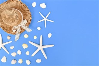 White starfish, seashells and summer straw hat on side of blue background with copy space