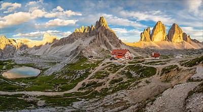 View of mountain hut Dreizinnenhuette and chapel with mountain lake rock massif Paternkofel and mountains three peaks in the sunset, panorama