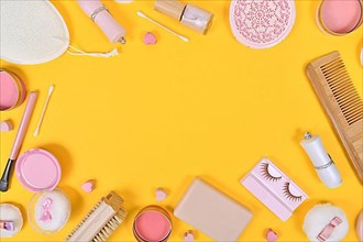 Various makeup beauty products like brushes, powder or lipstick surrounding yellow background with empty copy space