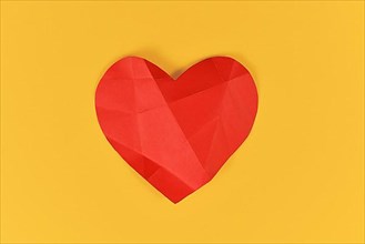 Red paper heart with folding lines on yellow background. Concept for broken or sick heart,
