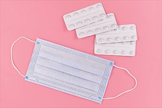 Medical face mask and pills in blister packs on pink background,