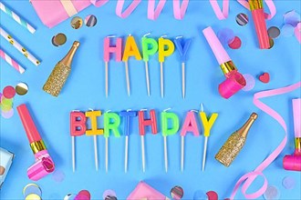 Party flat lay with Happy Birthday candles, confetti and paper streamers on blue background