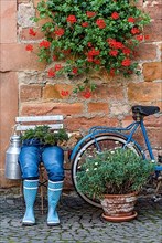 Curious decoration on a front door, blue jeans trousers in rubber boots with flower pot